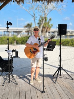 Michael McCormick performing with acoustic guitar on a sunny beachfront deck