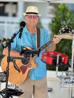 Michael McCormick smiling while singing and playing acoustic guitar at an outdoor event