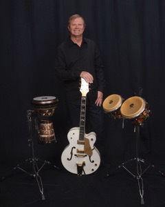 Michael McCormick standing with a white Gretsch guitar beside hand drums
