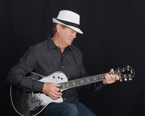 Michael McCormick playing an archtop electric guitar in a white fedora